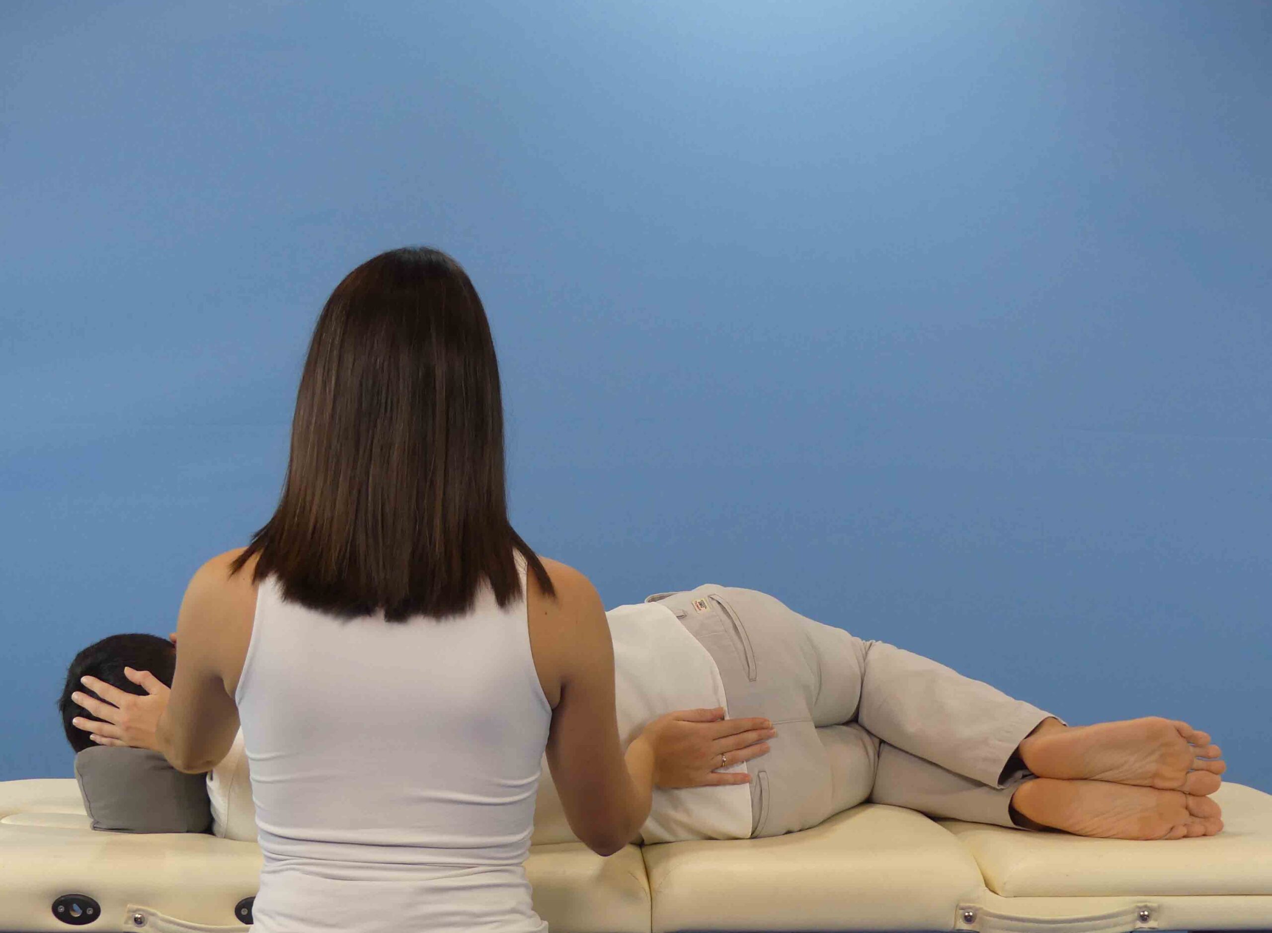 mujer practicando con hombre en camilla curso de terapia craneosacral practica de espalda en camilla del curso de terapia craneosacral
